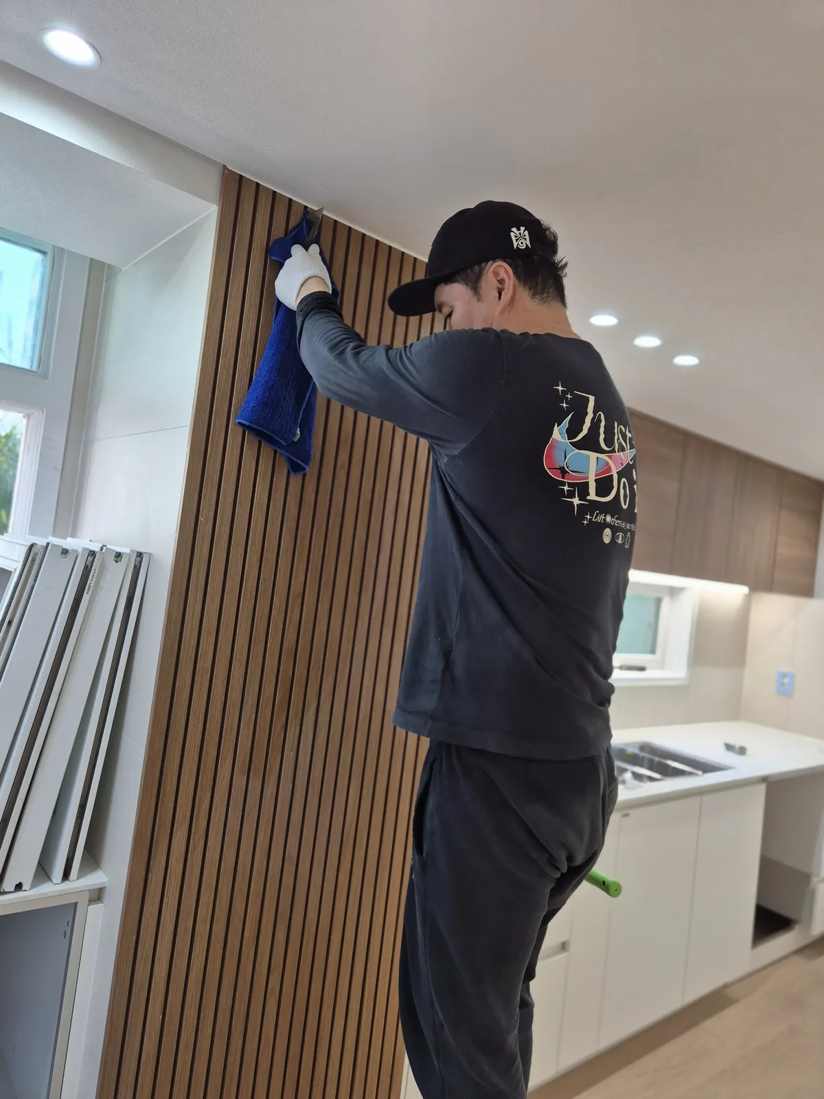 사다리 위에서 창가 쪽 벽면을 닦는 작업자, 분리된 창틀이 아래 놓여 있다